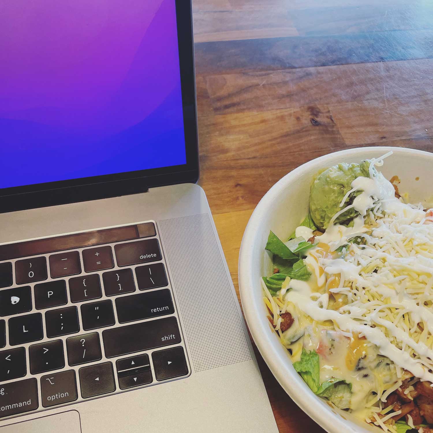 Open laptop on a table with a salad next to it.