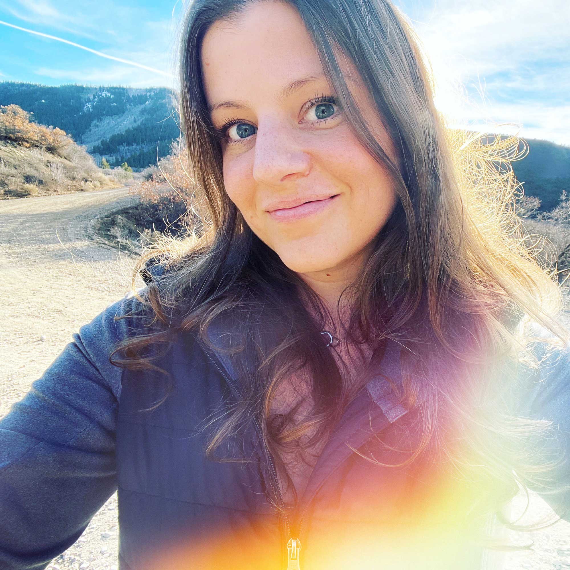 Stephenie Zamora, a 37 year old white woman with brown hair smiles in a selfie against a mountain backdrop.